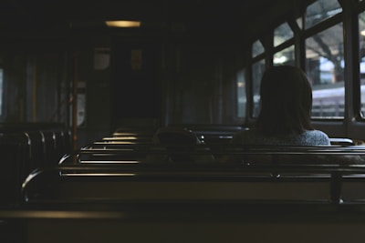 A dimly lit interior of a public transportation vehicle with empty seats and a single passenger sitting alone, gazing out of the window.