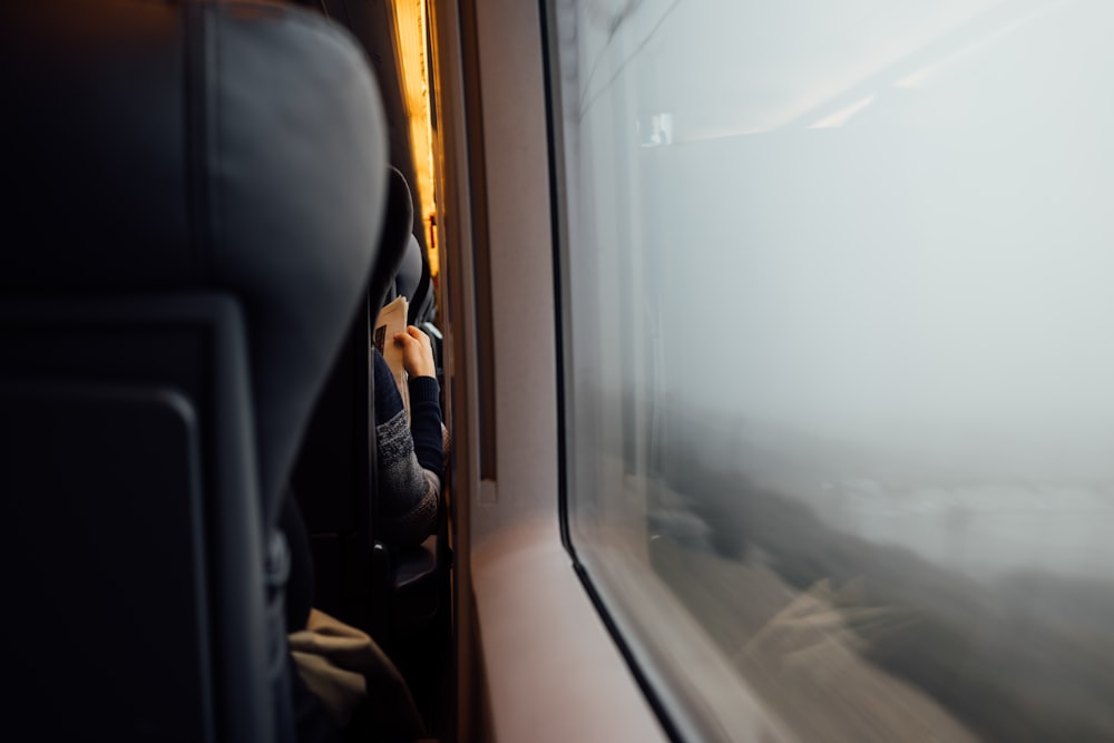 Pessoa lendo jornal por trás com encosto de cabeça em primeiro plano perto da janela do vagão do trem