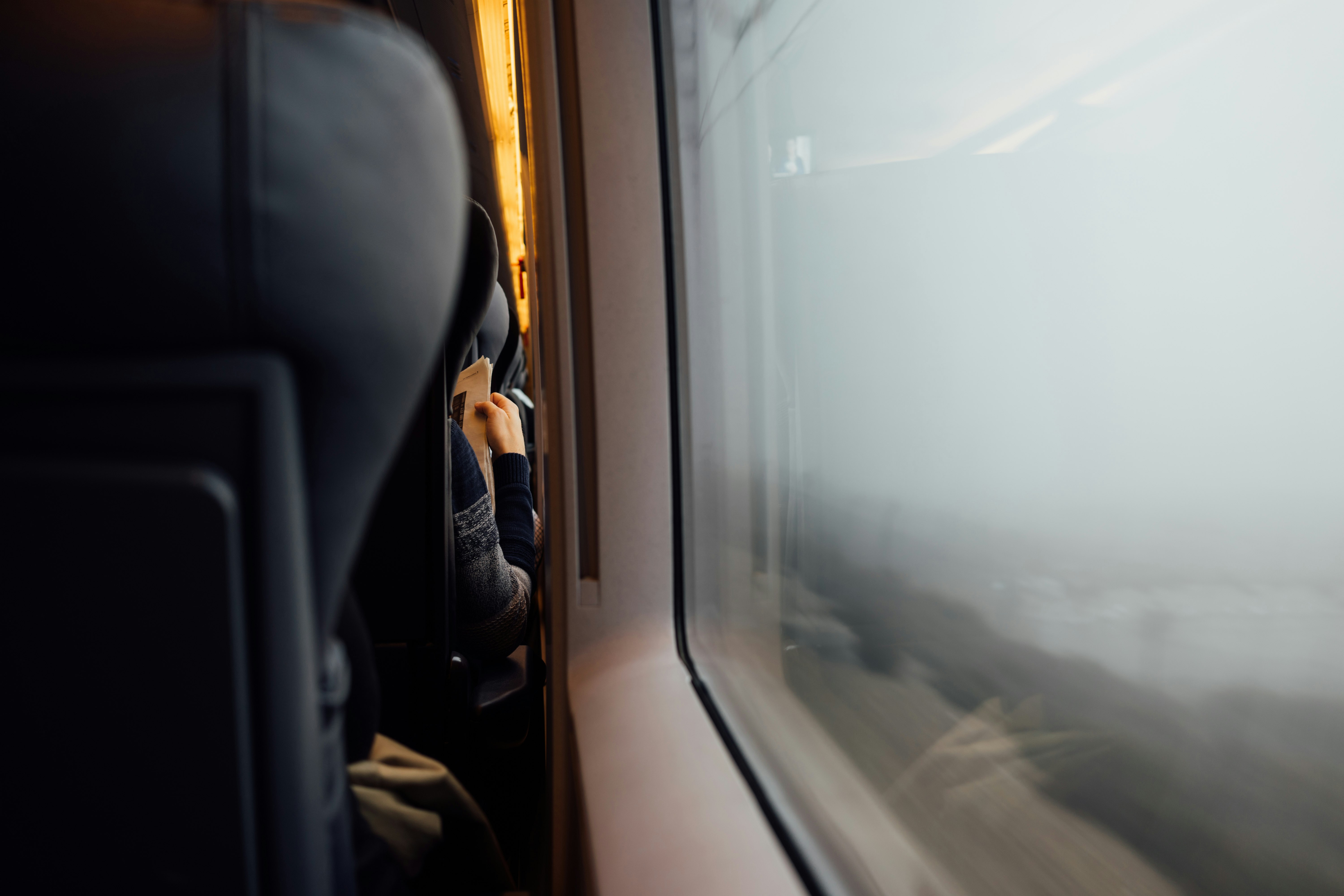 Person reading newspaper from behind with headrest in foreground near train carriage window