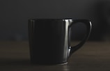 A sleek matte black coffee mug resting on a smooth wooden kitchen counter with soft natural light highlighting its minimalist design.