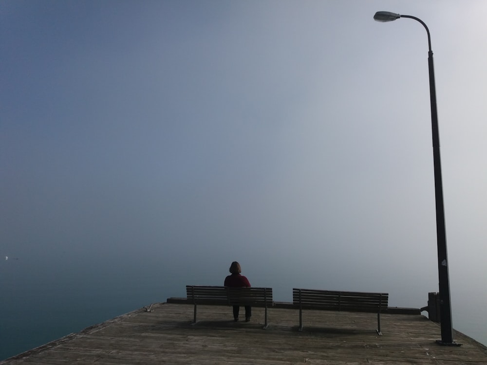 A large street light above a person sitting on one of two park benches.