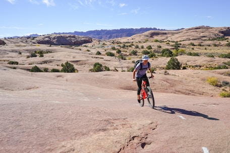 A mountain biker launching off a rugged rocky drop under a bright blue sky.