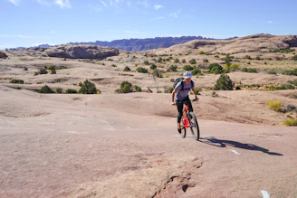 Mountain biker launching off a rocky trail with dust flying in the air under a cloudy sky.