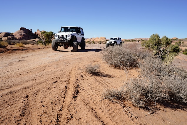 A rugged off-road motorcycle and 4x4 vehicle navigating through Moroccan desert terrain under a bright sky.
