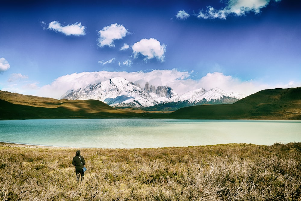 Persona de pie sobre la hierba verde con el cuerpo de agua verde tranquilo cerca de la vista de las montañas durante el día