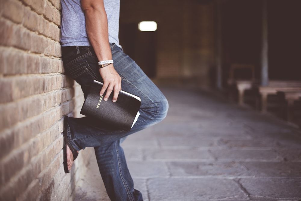 hombre sosteniendo la Santa Biblia apoyada en la pared de ladrillo