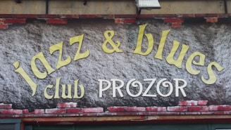 A sign features the words 'jazz & blues club PROZOR' in large, stylized letters. The background resembles a brick wall with some painted areas.