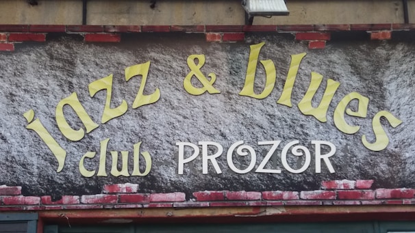 A sign features the words 'jazz & blues club PROZOR' in large, stylized letters. The background resembles a brick wall with some painted areas.