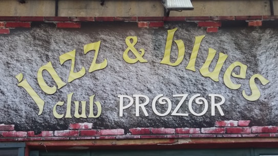 A sign features the words 'jazz & blues club PROZOR' in large, stylized letters. The background resembles a brick wall with some painted areas.