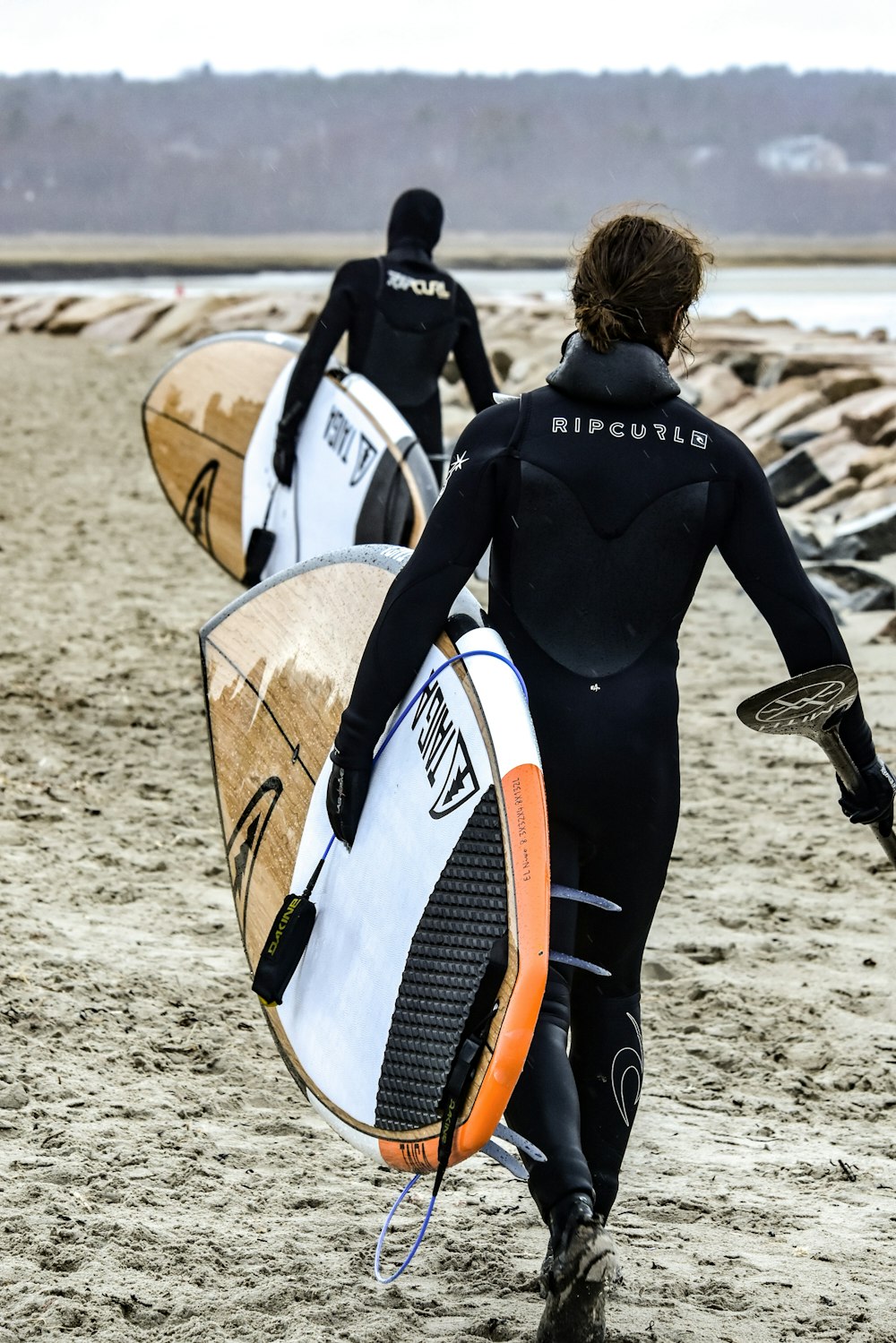 two person walking towards body of water while carrying surfboards