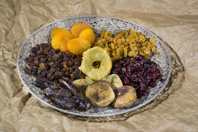 A rustic wooden basket filled with colorful dry fruits, millets, and spices arranged on a natural linen cloth.