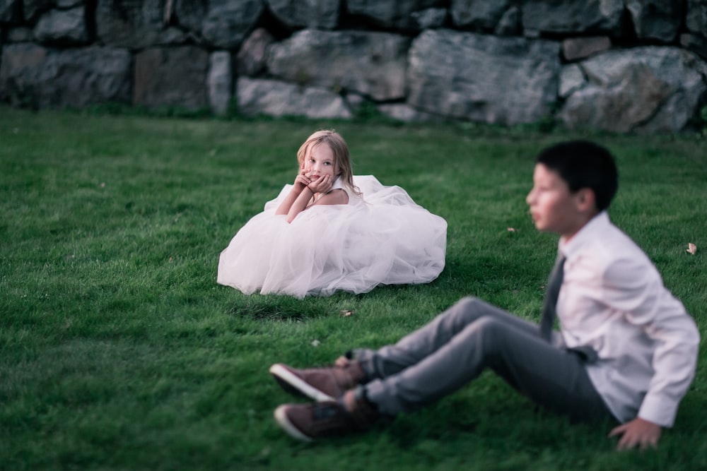 menina sentada na grama verde olhando para o menino sentado na grama verde