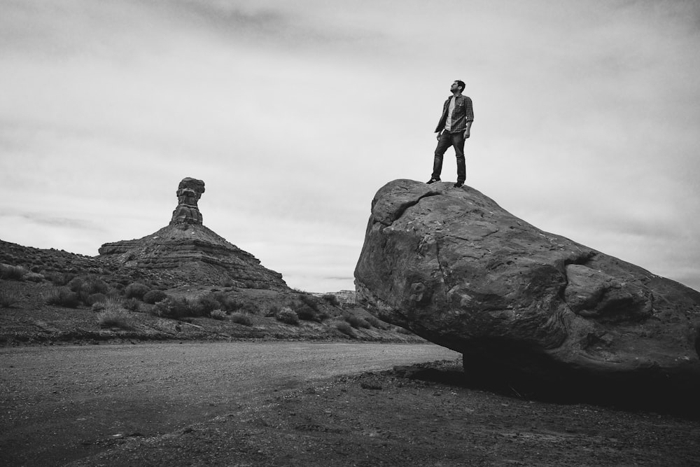 grayscale photo of man standing on rock formation