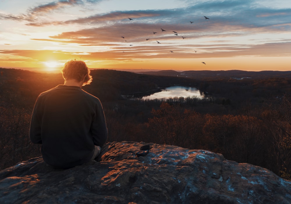 a person sitting on a rock looking at a lake