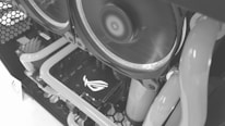 Close-up view of a computer's internal components featuring liquid cooling tubes and cooling fans. The ASUS Republic of Gamers (ROG) logo is visible on a hardware component, likely the graphics card. The image is in grayscale, highlighting the intricate design and layout of the PC internals.