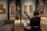 A person sits in an art gallery or museum, playing a guitar while facing a music stand with sheet music. The room has several paintings on the walls and sculptures inside glass cases. The lighting is focused on the artwork, highlighting the details and creating a cozy atmosphere.