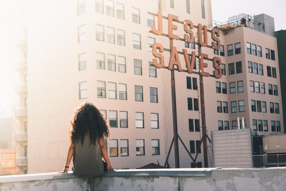 woman in gray top sitting on a building's edge