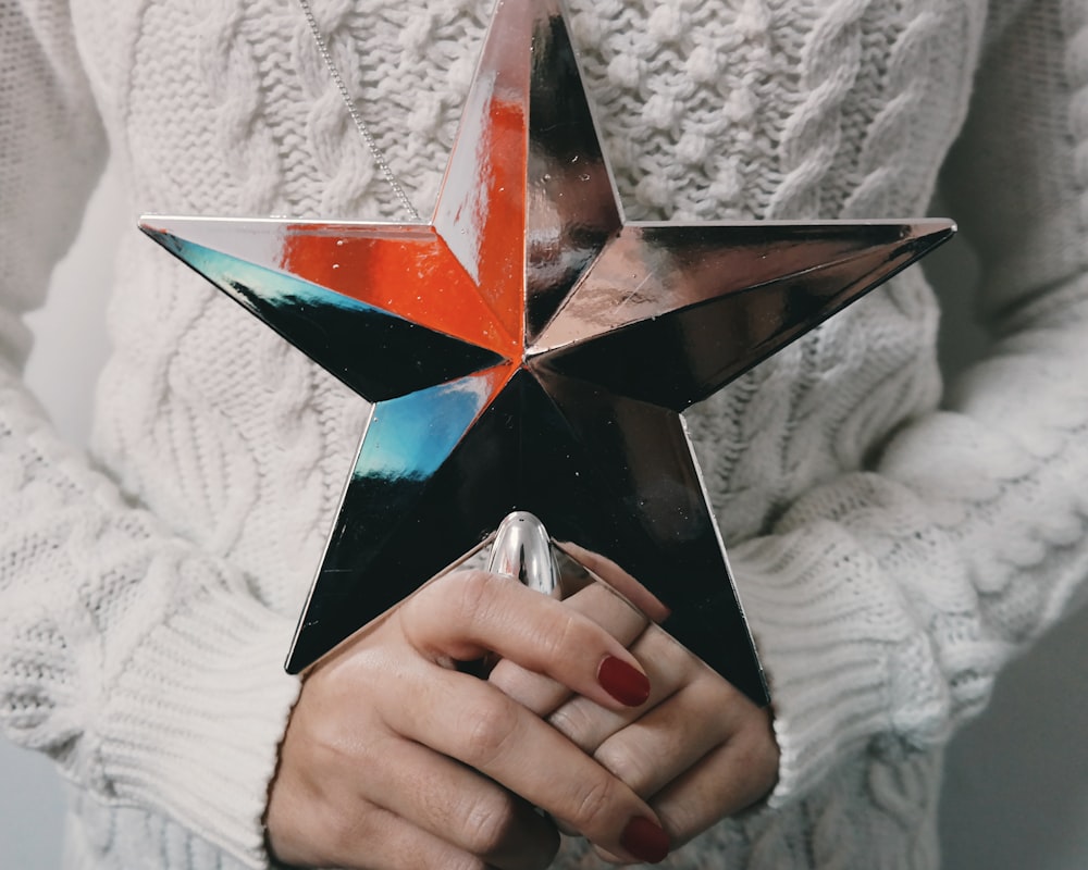 A person in a knitted sweater holding a star shaped tree topper.