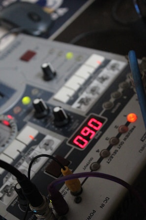 A close-up view of an electronic audio device featuring various knobs, buttons, and an illuminated red digital display showing the number 090. Several cables are plugged into the device, indicating it is powered and potentially in use.