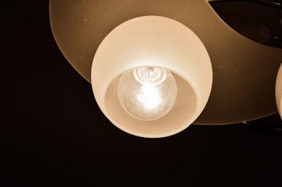 A close-up view of a lit ceiling lamp with a spherical frosted glass cover. The incandescent bulb inside is glowing brightly, casting light on the surrounding area.