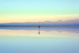 A serene view of the salt flats at sunrise with soft pink and orange hues reflecting on the water.