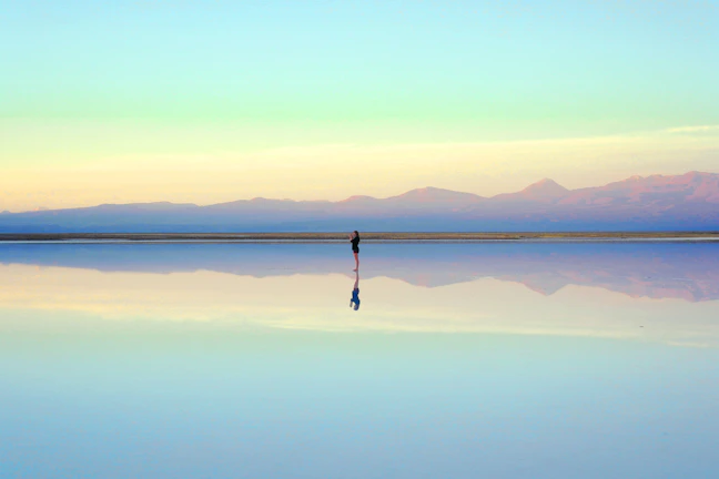 A serene view of the salt flats at sunrise with soft pink and orange hues reflecting on the water.