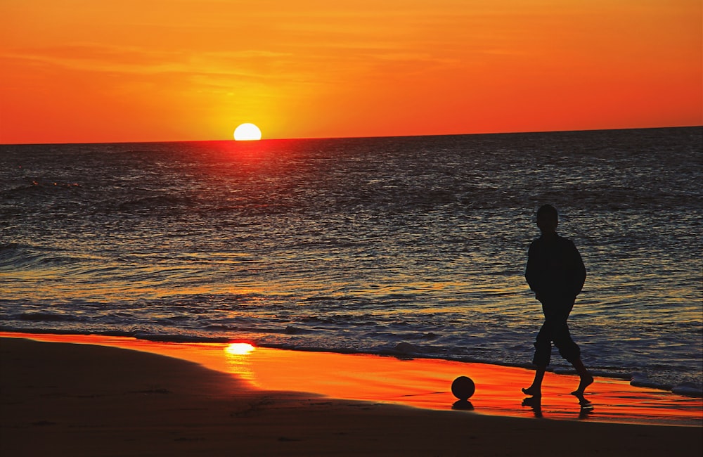 silhouette of man walking on beach during sunset