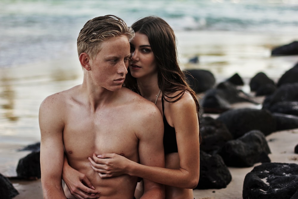 mujer con la parte superior del bikini de pie en la parte posterior del hombre en topless al lado de las rocas