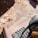 Wood shavings are scattered on a wooden surface, illuminated by sunlight. A power sander is positioned to the right, partially visible, suggesting a recent or ongoing sanding project. The scene is filled with the texture of sawdust and the contrasting smooth surface of sanded wood.