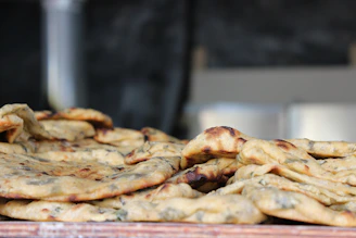 Close-up of a stack of golden-baked bhakhri flatbreads with scattered spices and herbs on a rustic wooden board.