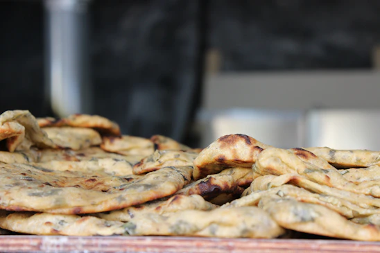 Close-up of a stack of golden-baked bhakhri flatbreads with scattered spices and herbs on a rustic wooden board.