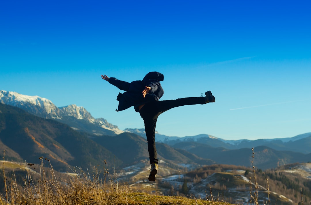 man in black jacket jumping on brown grass field during daytime