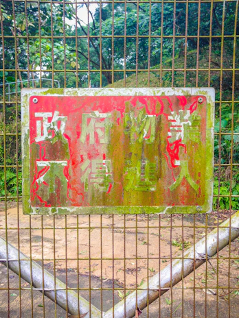 An aged metal garden sign with charming patina hanging on a wooden fence surrounded by greenery.