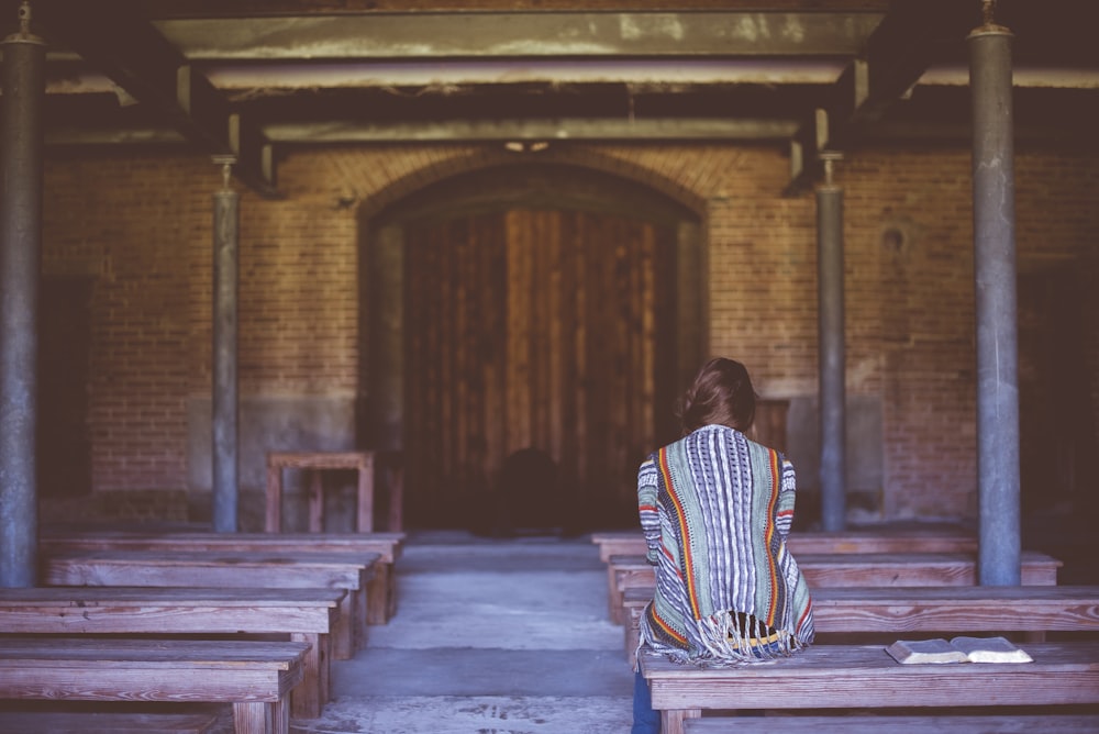 person in blue and orange top sitting on wooden bench inside building