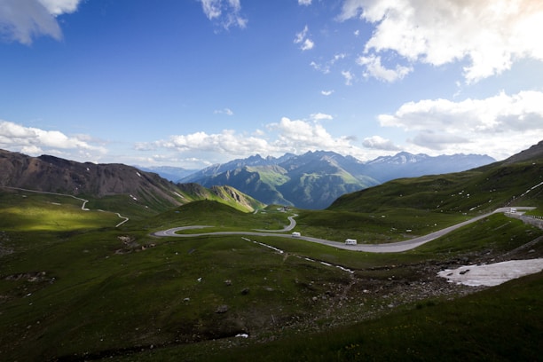 Scenic view of a winding road through lush green hills with a Bharat by Wheels vehicle in the distance.
