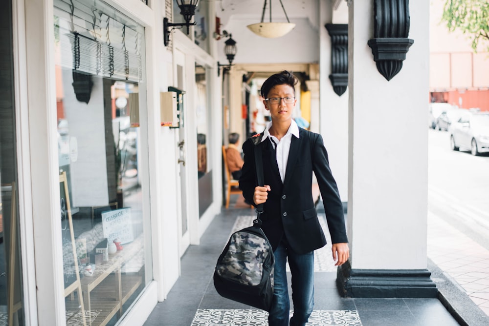 man carrying bag walking on black ceramic tiles during daytime