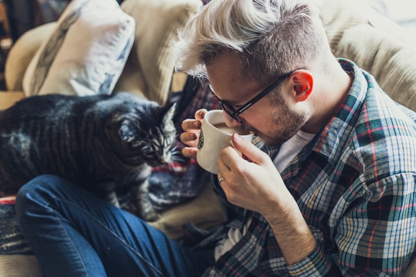 An unbothered white man sipping coffee with his cat