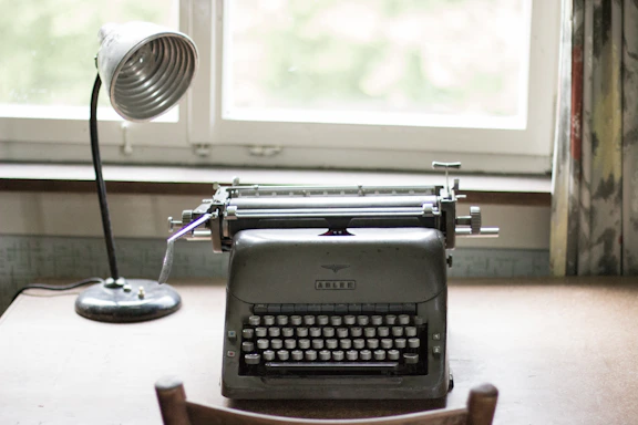 A cozy workspace with a vintage typewriter on a dark wooden desk, illuminated by soft warm light.