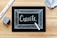 A blackboard with the word 'Create' written in white chalk, surrounded by a thin chalk-drawn border. A piece of white chalk and a ruler are placed on a wooden surface, alongside an eraser and a piece of fabric.