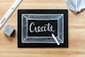 A blackboard with the word 'Create' written in white chalk, surrounded by a thin chalk-drawn border. A piece of white chalk and a ruler are placed on a wooden surface, alongside an eraser and a piece of fabric.