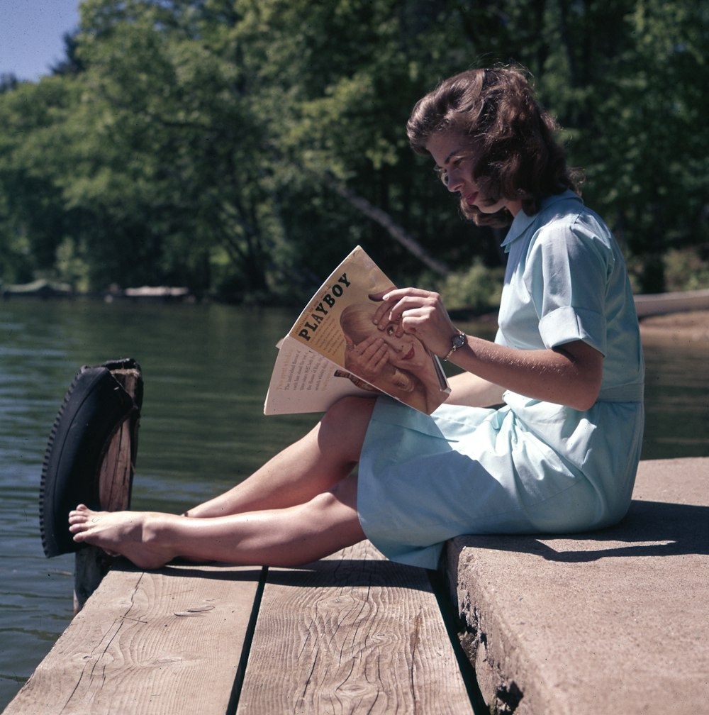 woman sitting while reading near body of water
