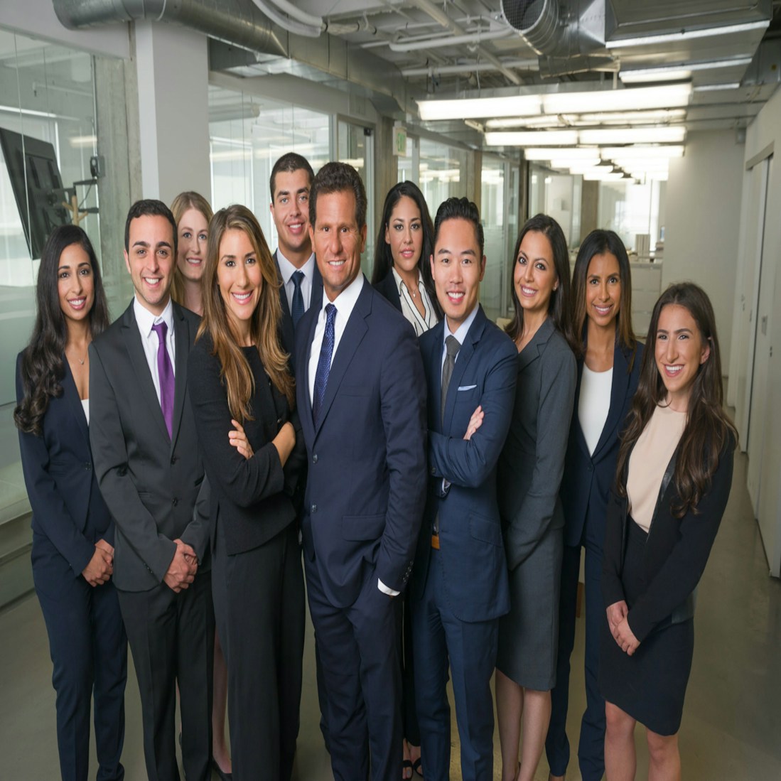 A group of ten professionally dressed individuals standing together in an office environment, smiling and exuding confidence.