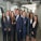 A group of ten professionally dressed individuals standing together in an office environment, smiling and exuding confidence.