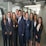 A group of ten professionally dressed individuals standing together in an office environment, smiling and exuding confidence.