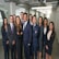 A group of ten professionally dressed individuals standing together in an office environment, smiling and exuding confidence.