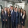 A group of ten professionally dressed individuals standing together in an office environment, smiling and exuding confidence.