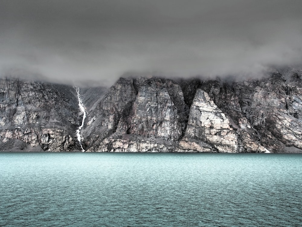 gray cliff beside body of water covered by fog