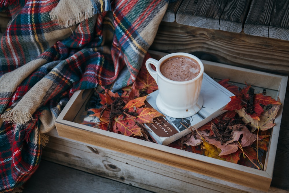 mug of chocolate drink on top of book beside fringed shawl