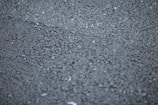 A close-up view of a rough asphalt surface, displaying a textured pattern made up of small, irregularly shaped stones and gravel.