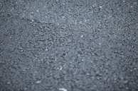 Close-up of hands spreading asphalt evenly with a rake, showing texture detail.